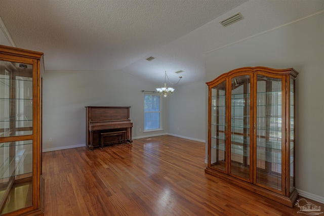 interior space with a notable chandelier, dark hardwood / wood-style floors, a textured ceiling, and vaulted ceiling