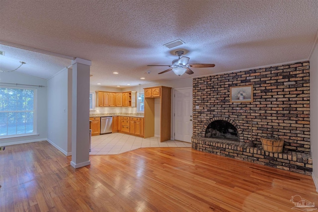 unfurnished living room featuring ceiling fan, light wood-type flooring, a textured ceiling, and a brick fireplace