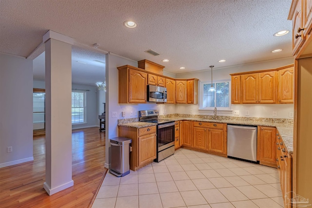 kitchen featuring hanging light fixtures, light hardwood / wood-style flooring, a textured ceiling, light stone counters, and stainless steel appliances