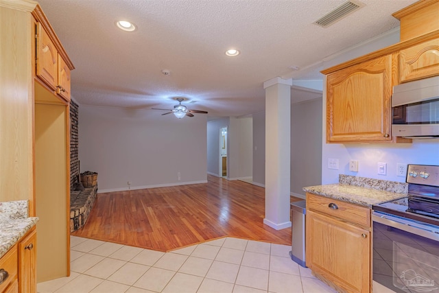 kitchen featuring ceiling fan, stainless steel appliances, light stone counters, a textured ceiling, and light tile patterned floors