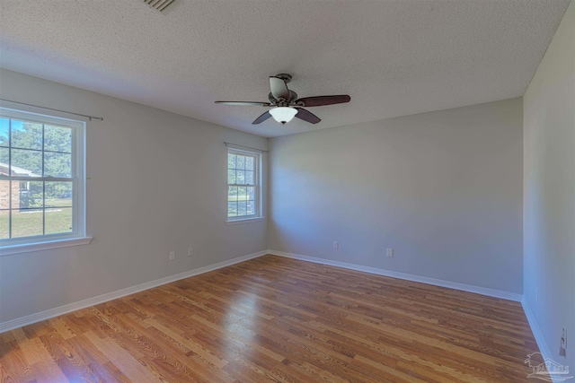 spare room featuring a healthy amount of sunlight, ceiling fan, wood-type flooring, and a textured ceiling