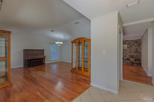 unfurnished living room featuring vaulted ceiling, light hardwood / wood-style flooring, a notable chandelier, and a textured ceiling