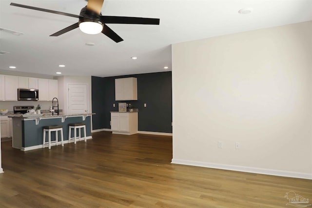 kitchen with sink, white cabinetry, wood-type flooring, appliances with stainless steel finishes, and a kitchen breakfast bar