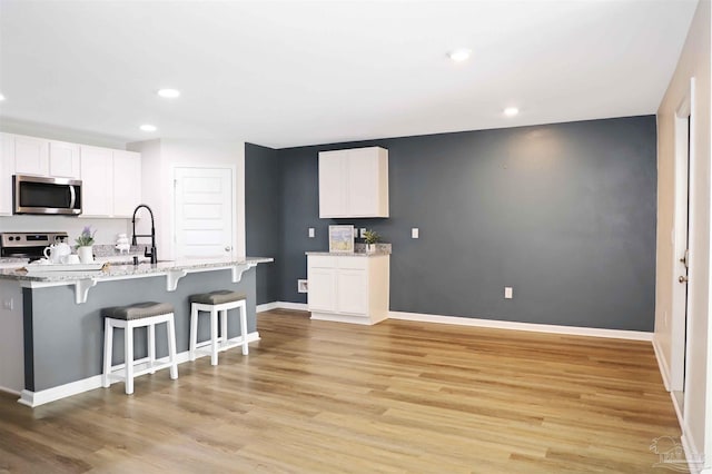 kitchen featuring light hardwood / wood-style flooring, appliances with stainless steel finishes, light stone counters, white cabinets, and a kitchen bar