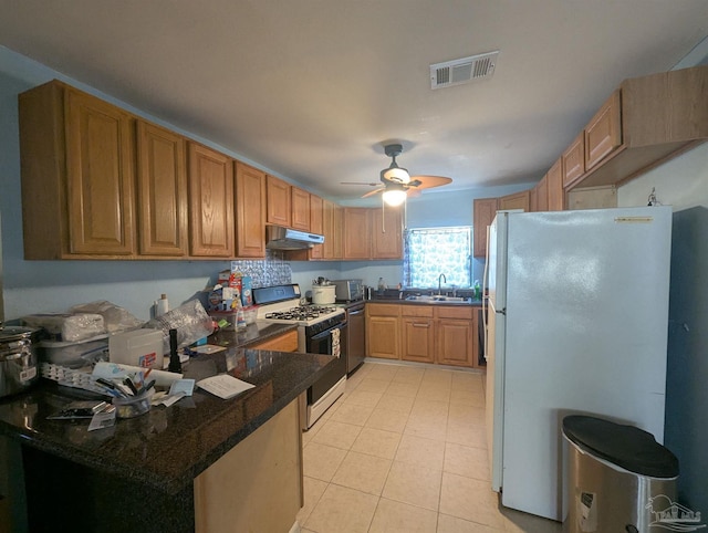 kitchen featuring visible vents, a sink, under cabinet range hood, gas range oven, and freestanding refrigerator