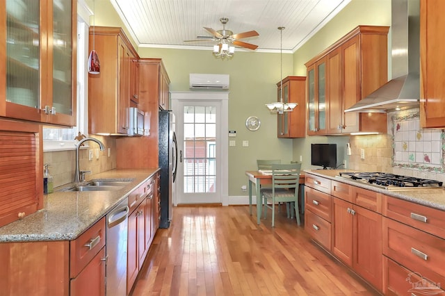 kitchen featuring brown cabinets, a wall unit AC, stainless steel appliances, a sink, and wall chimney range hood