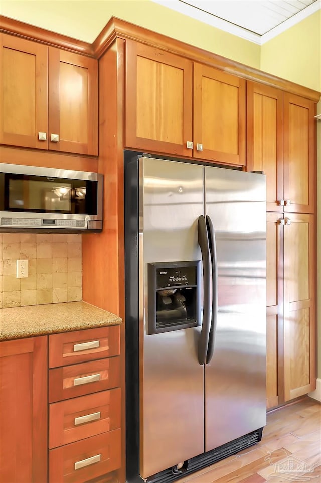 kitchen with light wood finished floors, appliances with stainless steel finishes, brown cabinets, light stone countertops, and backsplash