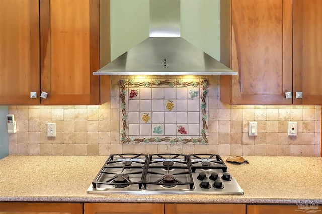 kitchen with wall chimney range hood, stainless steel gas stovetop, decorative backsplash, and brown cabinetry