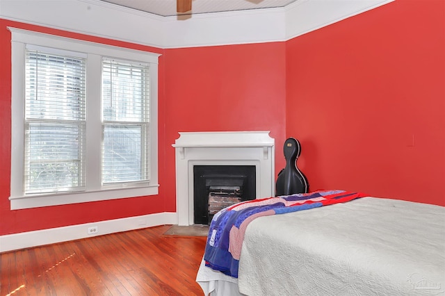 bedroom featuring a fireplace with flush hearth, wood-type flooring, baseboards, and a ceiling fan