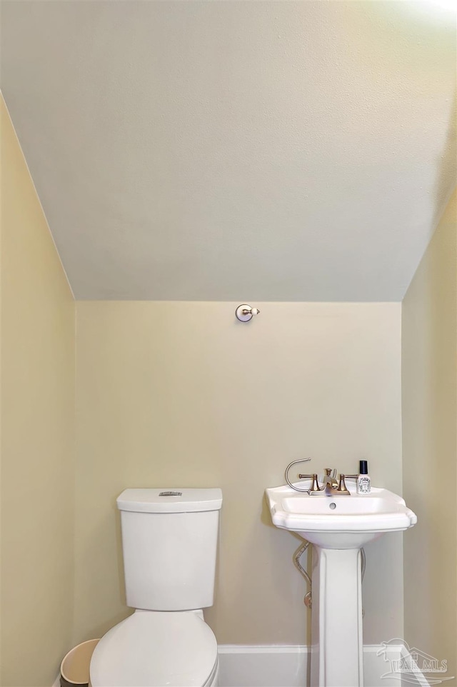 half bath with vaulted ceiling, toilet, and baseboards