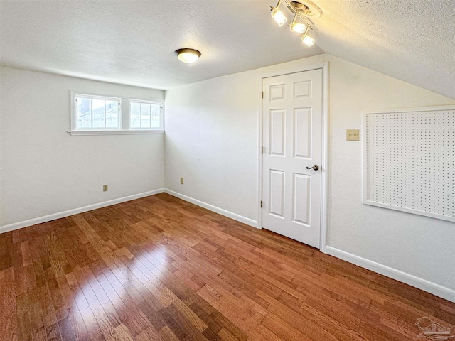 interior space featuring a textured ceiling, lofted ceiling, hardwood / wood-style flooring, and baseboards