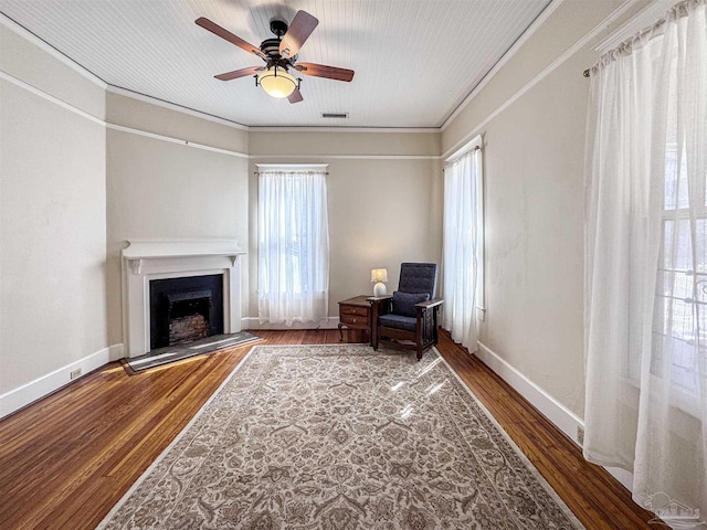 living area featuring a fireplace with raised hearth, baseboards, wood finished floors, and crown molding