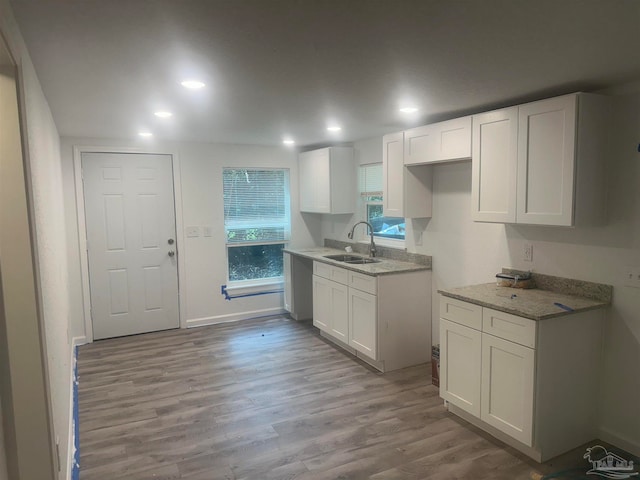 kitchen with white cabinetry, sink, light hardwood / wood-style floors, and light stone counters