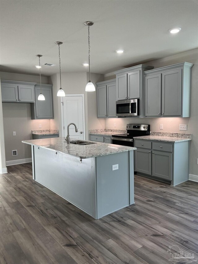 kitchen with dark wood-type flooring, appliances with stainless steel finishes, sink, decorative light fixtures, and a center island with sink