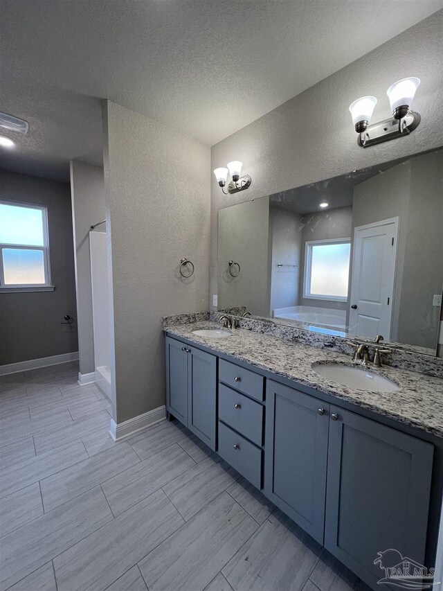 bathroom with tile patterned floors, a textured ceiling, a healthy amount of sunlight, and double sink vanity