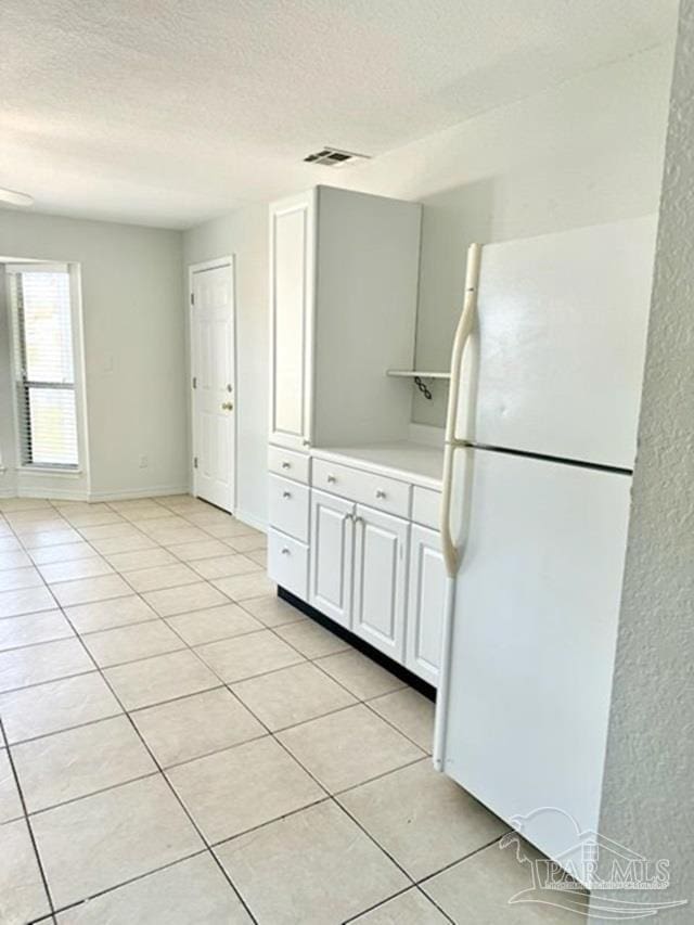 kitchen featuring white cabinets, white fridge, light tile patterned floors, and a textured ceiling