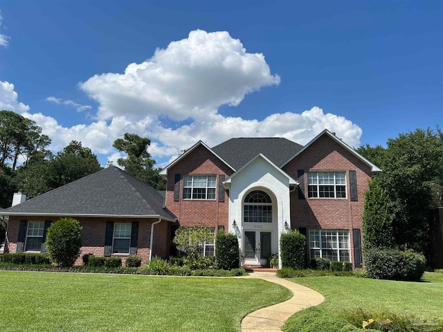 traditional-style house with brick siding, french doors, a chimney, and a front lawn