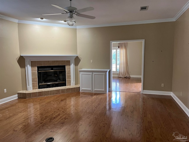 unfurnished living room with visible vents, baseboards, a tiled fireplace, ornamental molding, and wood finished floors