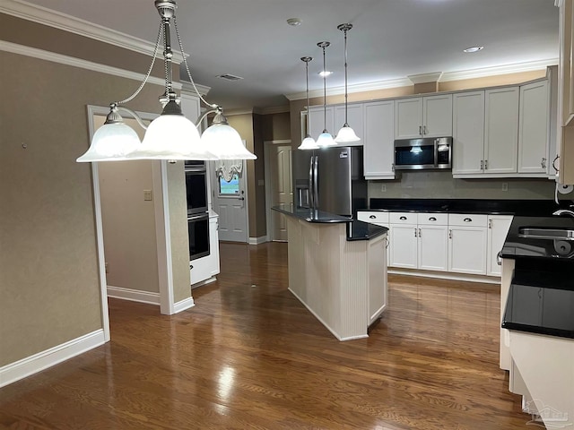 kitchen with a kitchen island, dark wood finished floors, ornamental molding, appliances with stainless steel finishes, and dark countertops