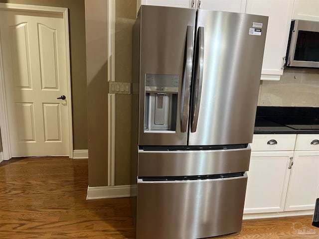 details with wood finished floors, baseboards, white cabinets, appliances with stainless steel finishes, and dark countertops