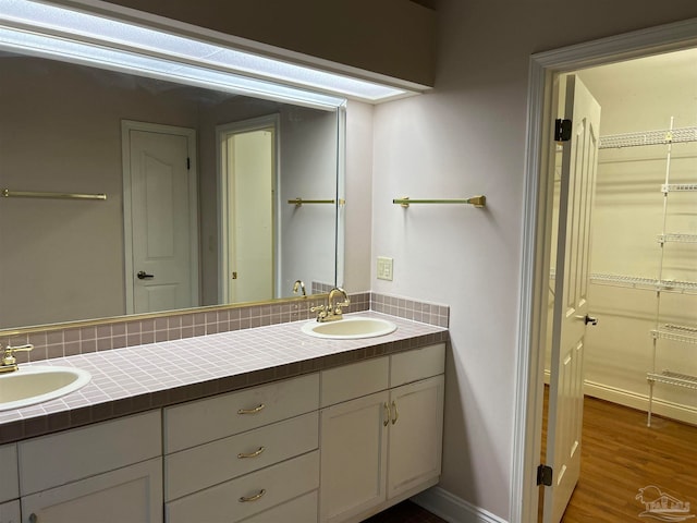 bathroom featuring a sink, baseboards, wood finished floors, and double vanity