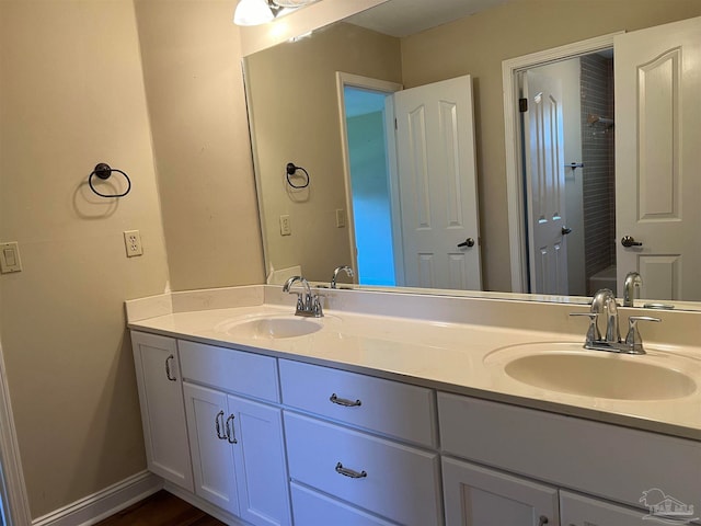 bathroom with double vanity, walk in shower, baseboards, and a sink