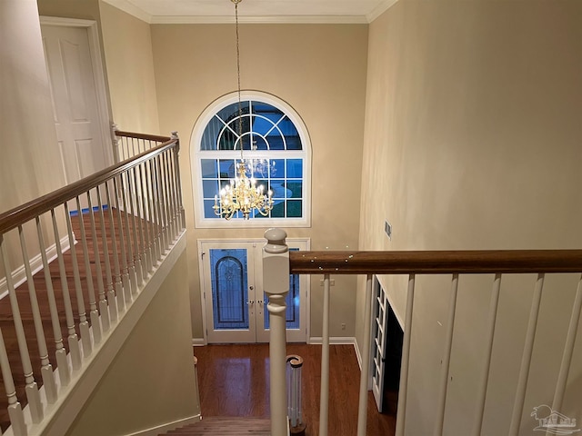 staircase with wood finished floors, baseboards, a high ceiling, crown molding, and a notable chandelier