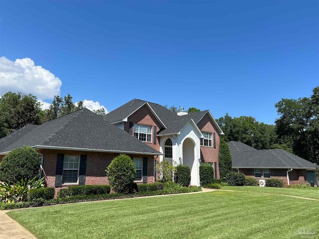 view of front facade featuring brick siding, a chimney, a front lawn, and a shingled roof