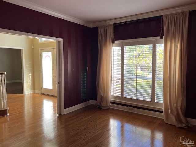 unfurnished room with crown molding, wood finished floors, a healthy amount of sunlight, and baseboards