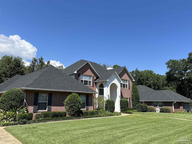 view of front of house featuring brick siding, a chimney, a front yard, and a shingled roof