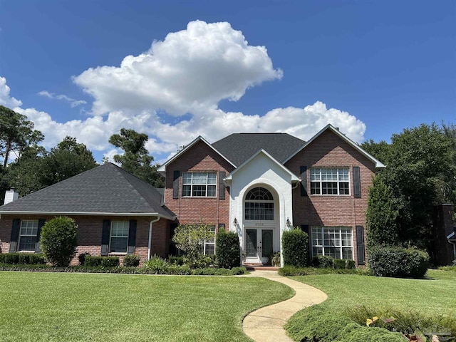 traditional-style home with a front yard, roof with shingles, a chimney, french doors, and brick siding