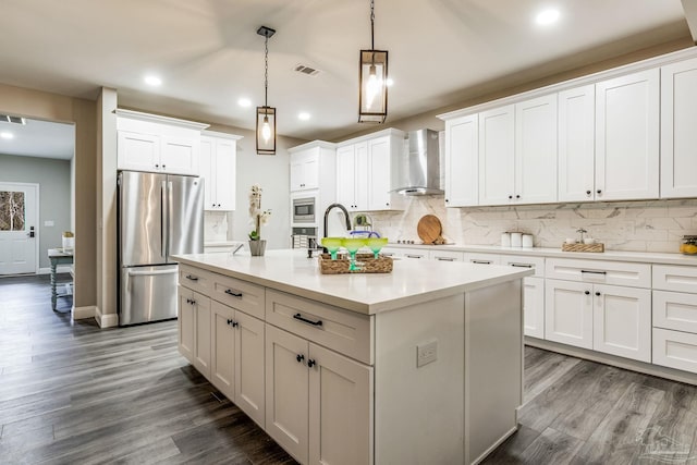 kitchen with white cabinetry, stainless steel appliances, wall chimney exhaust hood, and a center island with sink