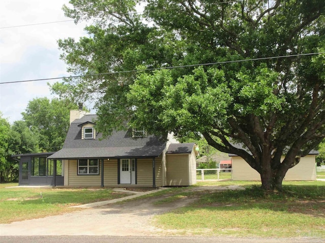 view of front of house with dirt driveway, a chimney, a shingled roof, a sunroom, and a front yard