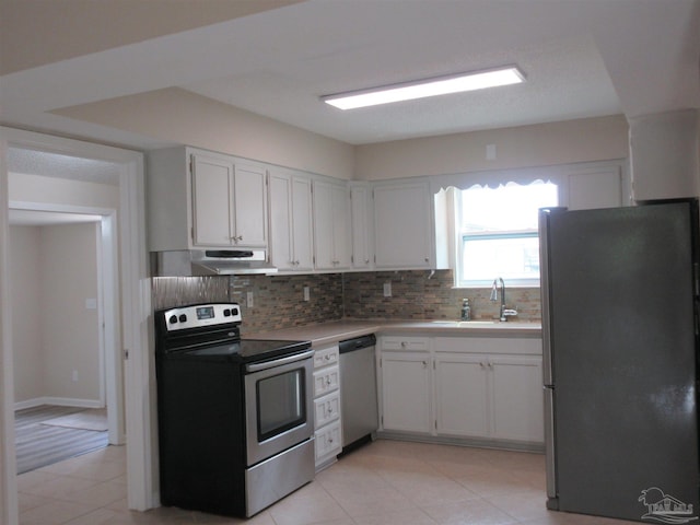 kitchen with under cabinet range hood, light tile patterned floors, a sink, tasteful backsplash, and appliances with stainless steel finishes