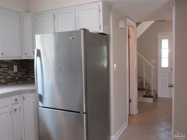kitchen with white cabinets, light countertops, light tile patterned flooring, freestanding refrigerator, and tasteful backsplash