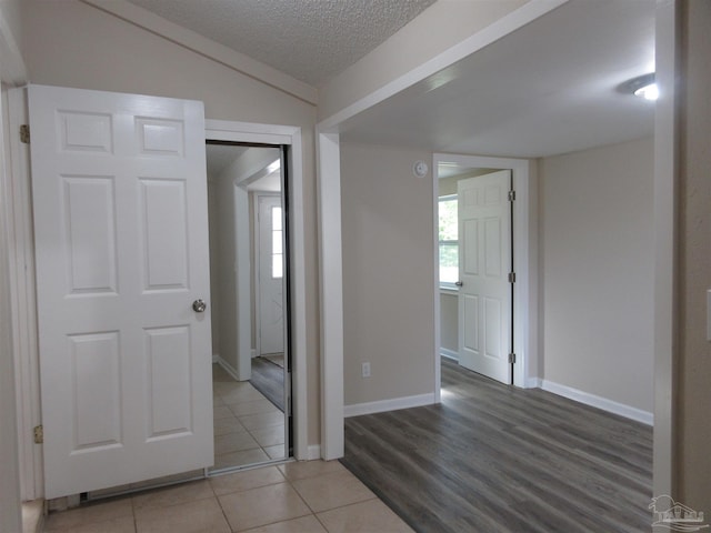 empty room with baseboards, vaulted ceiling, a textured ceiling, and light tile patterned floors