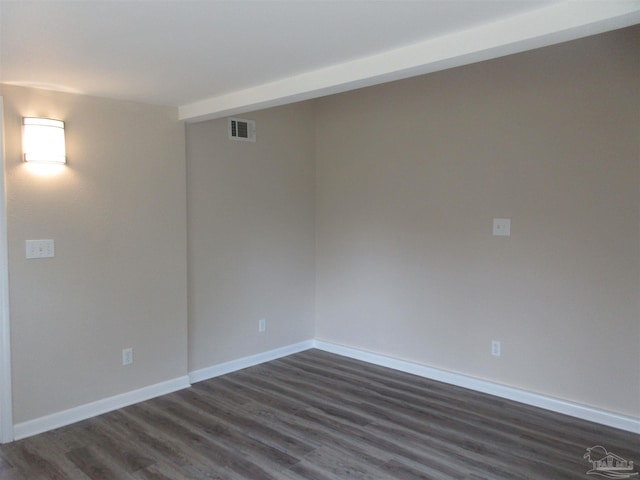 spare room featuring dark wood-type flooring, visible vents, and baseboards