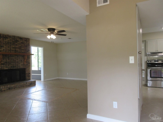 unfurnished living room with visible vents, light tile patterned floors, baseboards, a brick fireplace, and ceiling fan