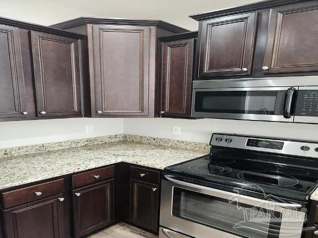 kitchen with appliances with stainless steel finishes, light stone counters, and dark brown cabinetry