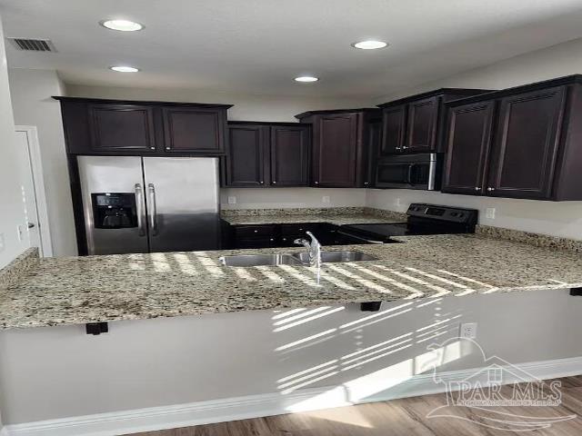 kitchen featuring stainless steel appliances, light stone countertops, sink, and hardwood / wood-style floors