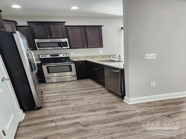 kitchen featuring sink, stainless steel appliances, light stone counters, dark brown cabinetry, and light hardwood / wood-style floors