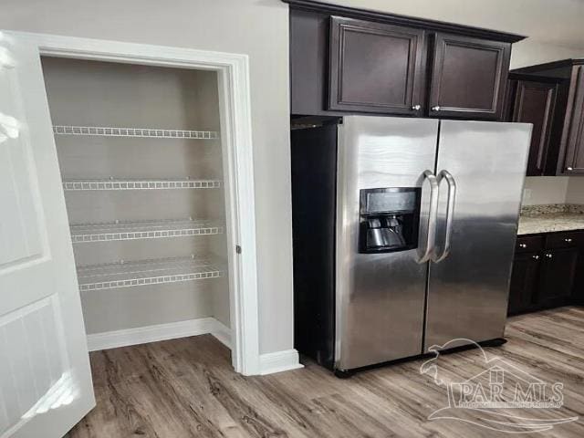 kitchen featuring light stone countertops, stainless steel fridge with ice dispenser, dark brown cabinets, and light hardwood / wood-style flooring