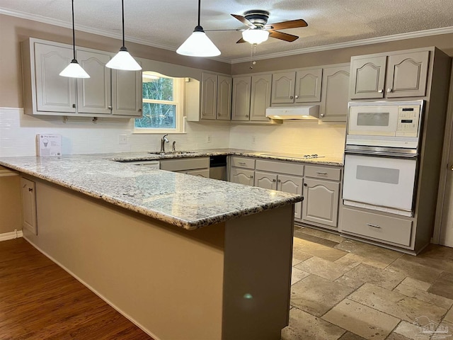 kitchen featuring white appliances, sink, light stone counters, and kitchen peninsula