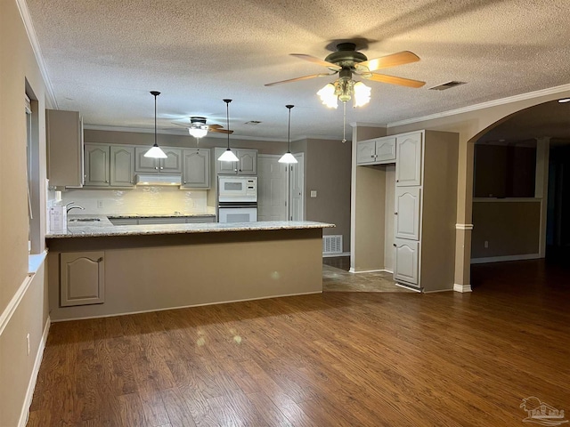 kitchen featuring white microwave, ornamental molding, kitchen peninsula, decorative backsplash, and hanging light fixtures