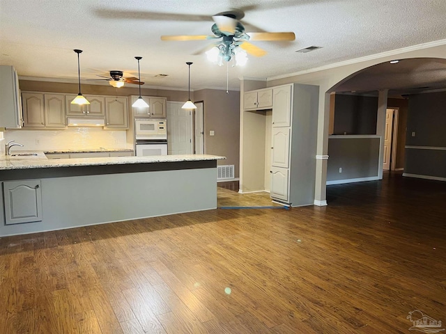 kitchen featuring white microwave, stainless steel oven, a textured ceiling, light stone counters, and decorative backsplash