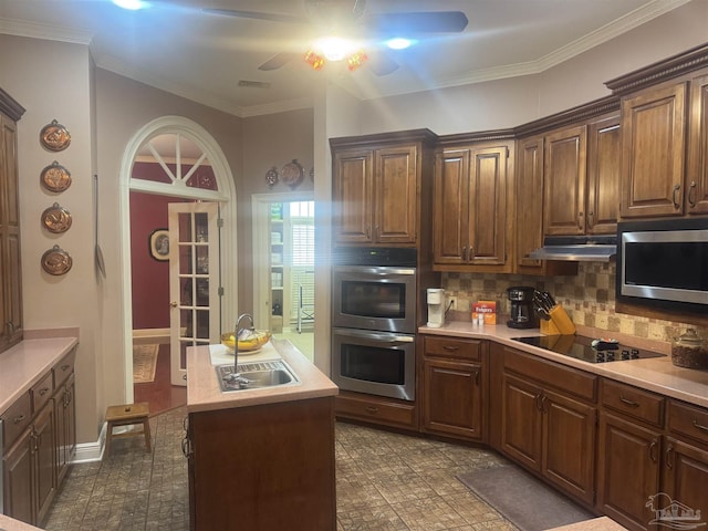 kitchen with appliances with stainless steel finishes, ornamental molding, a kitchen island, ceiling fan, and decorative backsplash