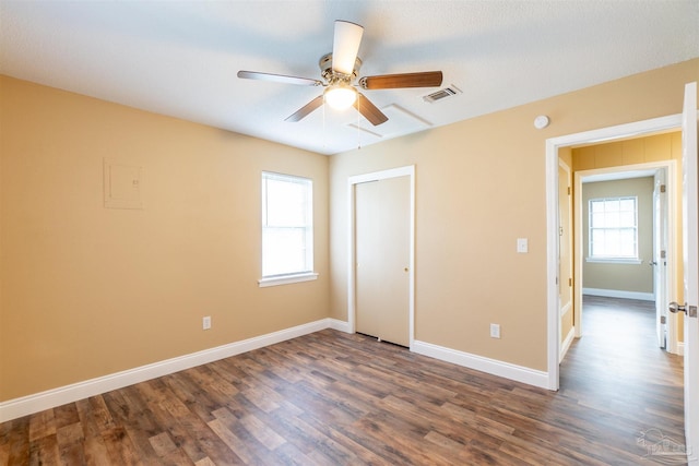 unfurnished bedroom featuring multiple windows, dark hardwood / wood-style flooring, ceiling fan, and a closet