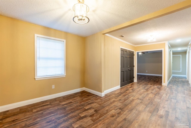 unfurnished room featuring a textured ceiling, crown molding, dark hardwood / wood-style flooring, and a notable chandelier