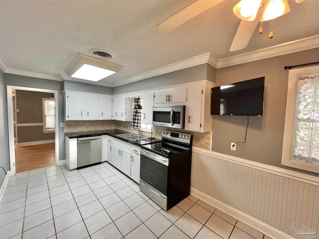 704 E Horner St, Atmore, AL 36502 - kitchen featuring appliances with stainless steel finishes, light tile patterned floors, white cabinets, wainscoting, and ornamental molding