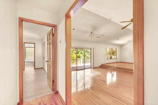 hall with light wood-type flooring and a textured ceiling